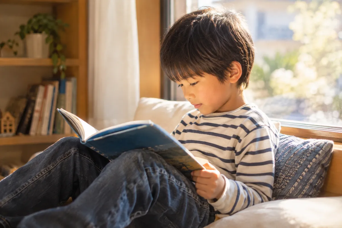 男の子が窓辺でひとりで本を読んでいる写真